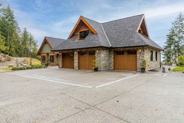 Stone and wood garage with three doors beside a green house in a forested area.