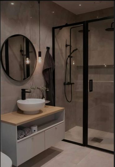 Modern bathroom with black-framed shower and round mirror.