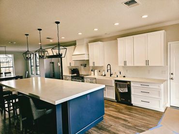Modern kitchen with white cabinets and a large blue island under geometric pendant lights.