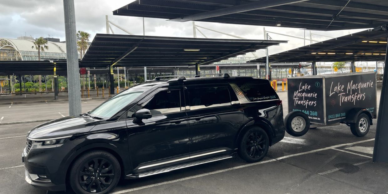 Black SUV towing a trailer with Lake Macquarie Transfers signage.