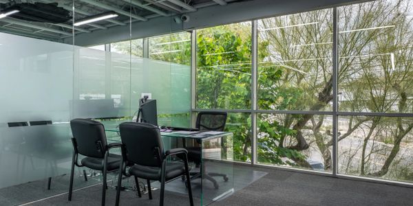 Modern office meeting room with glass walls and black chairs.