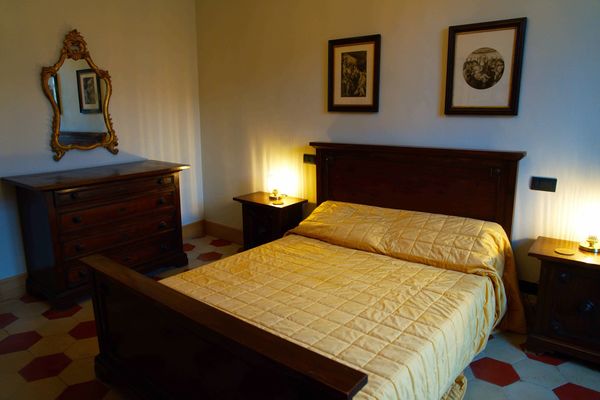 Antique bed in a renovated bedroom with original hexagonal floor tiles, antique prints and furnitureu