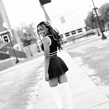 Cheerleader in uniform joyfully raising her pom-pom outdoors.