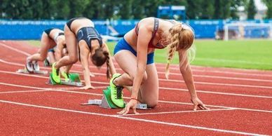 Female athletes poised at starting blocks on a running track.