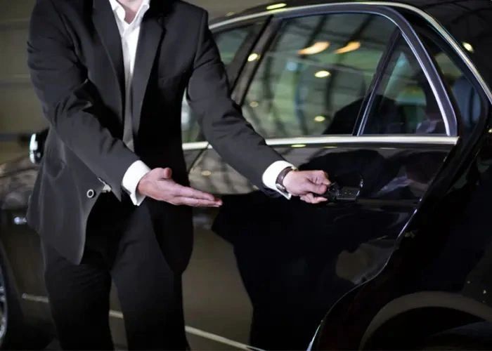 A person in a suit opening a car door.