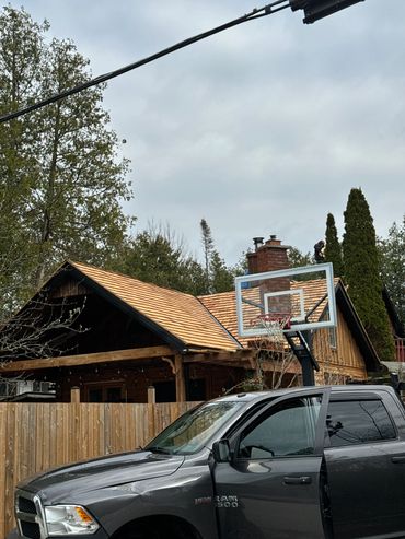 A gray Ram 1500 truck parked near a wooden house with a basketball hoop.