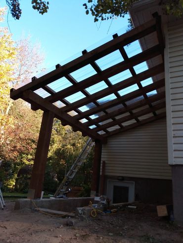 Wooden pergola with transparent roof panels attached to a house.