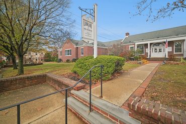 Exterior of a brick library building with a sign and autumn trees.