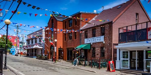Colorful flags decorate a sunny street with brick and wooden buildings.