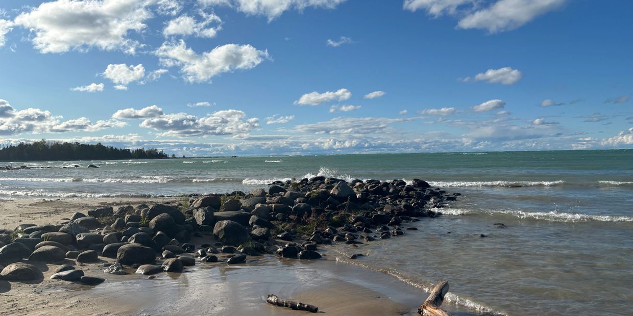 Rocky shoreline with gentle waves under a partly cloudy blue sky.