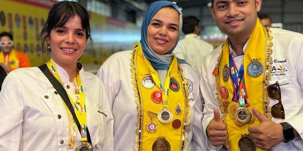 Three award-winning chefs proudly display their medals and yellow sashes indoors.