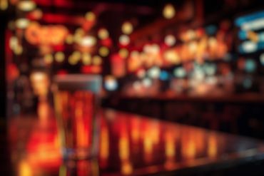Blurred image of a bar counter with warm lights and a glass.