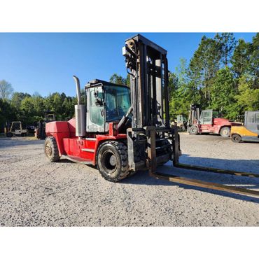 Large red forklift parked on gravel with trees in the background.