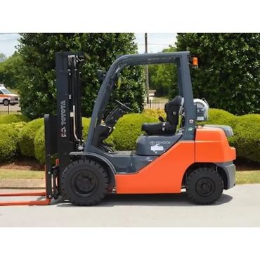 Orange and gray Toyota forklift parked outdoors near green bushes.