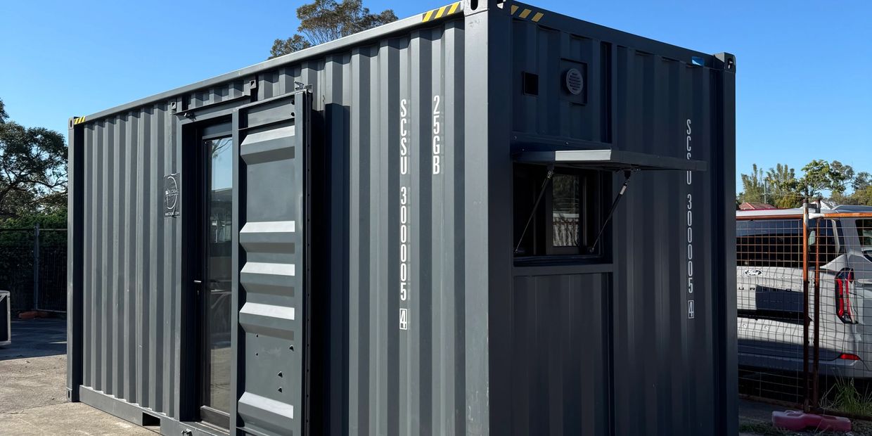 A dark gray shipping container with windows and a door on a concrete surface.