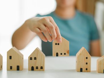 Person arranging wooden house models on a table.