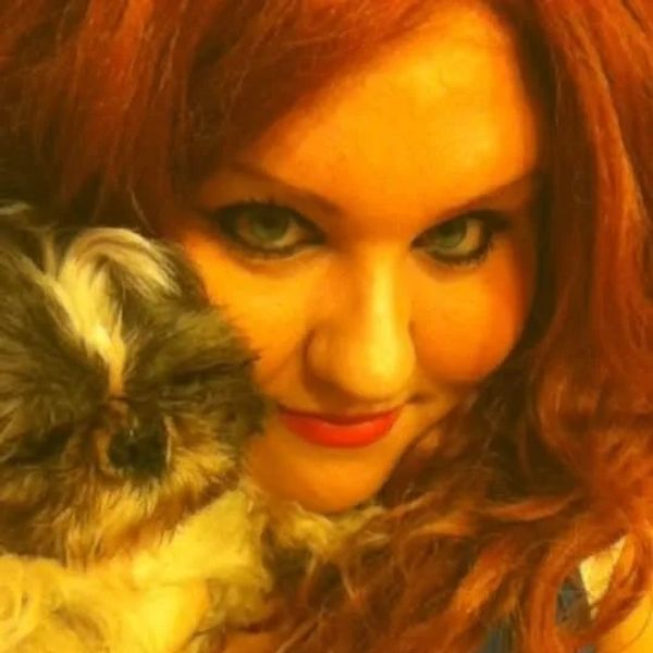 Woman with red hair holding a fluffy small dog close to her face.