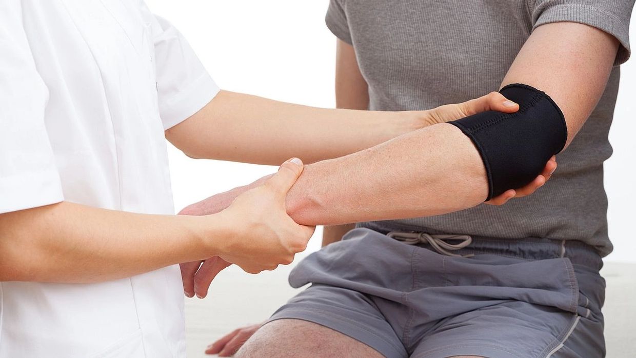 A healthcare worker supports a man's injured arm with an elbow brace.