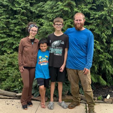 A family of four standing in front of green bushes, smiling.