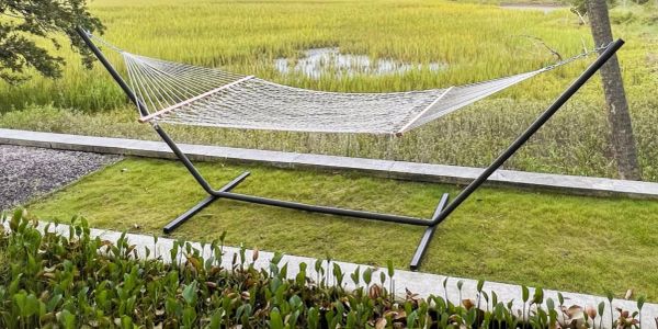 Empty hammock with metal stand on grass overlooking a marsh.