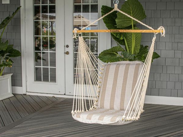 Striped cushioned hammock chair hanging on a porch with plants.