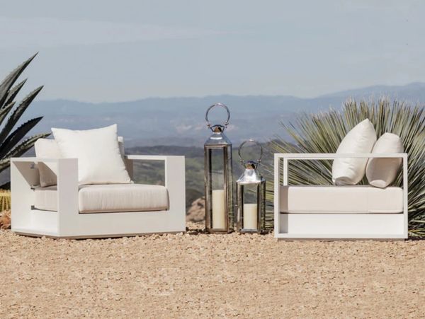 Modern white outdoor armchairs with cushions and decorative lanterns on a desert landscape.