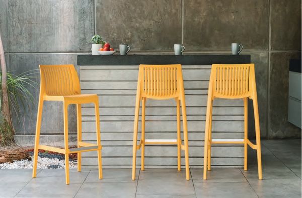 Three yellow bar stools in front of a modern concrete bar counter.