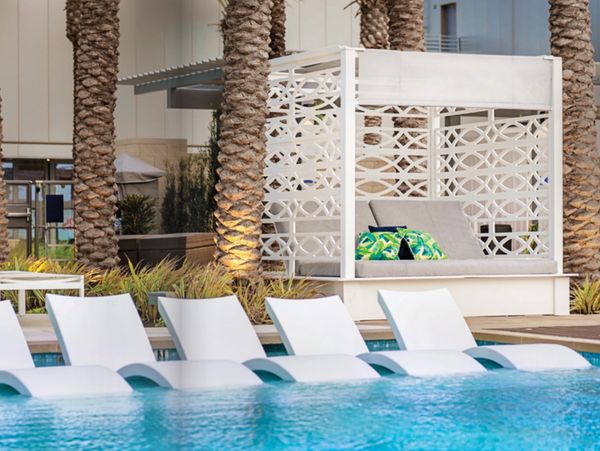 Modern poolside lounge area with white loungers and a cabana.