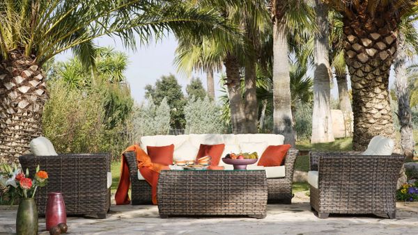 Cozy outdoor seating area with wicker furniture and orange cushions under palm trees.