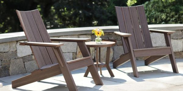 Two wooden Adirondack chairs with a small table and flowers between them.