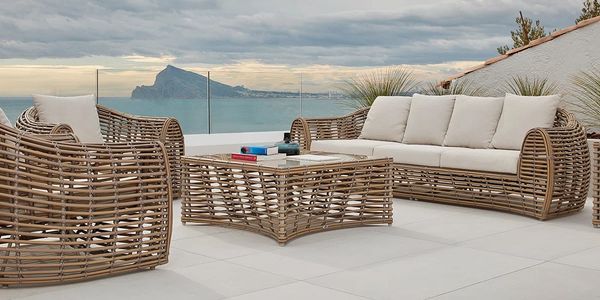 Outdoor wicker patio furniture with beige cushions overlooking a scenic coastal view.