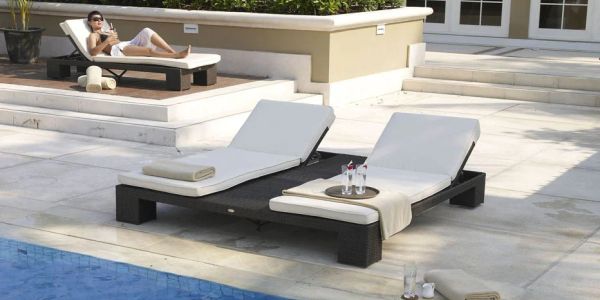 Two white loungers beside a pool with a woman relaxing on one.