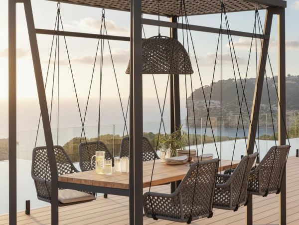 Outdoor dining area with hanging chairs and scenic ocean view at sunset.