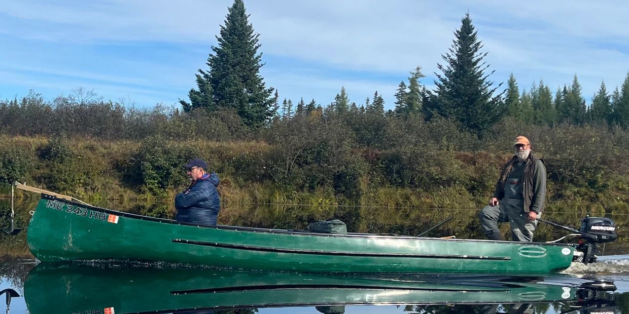 Two men fishing on a calm lake in a green canoe with clear sky.
