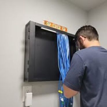 Technician organizing blue network cables inside a wall-mounted panel.