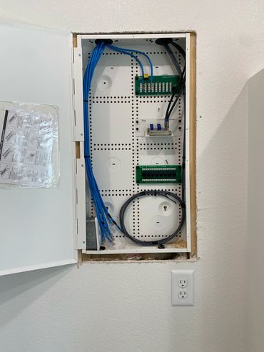 Open wall panel with organized blue and black cables and circuit boards.