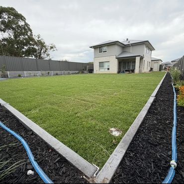 A modern two-story house with a large, well-manicured backyard enclosed by fences.