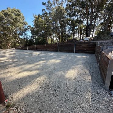 A gravel driveway bordered by wooden retaining walls under tall trees.