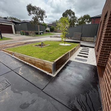 Neat front yard with raised grass bed and stepping stones on white pebbles.