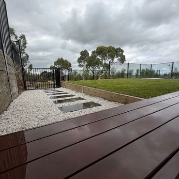 Modern backyard with a wet wooden deck and stone pathway under cloudy skies.