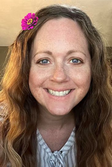 A smiling woman with blue eyes, freckles, and a flower in her long hair.