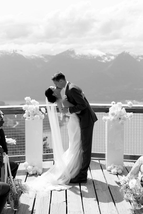 Bride and groom sharing a kiss on a scenic mountain deck during their wedding.