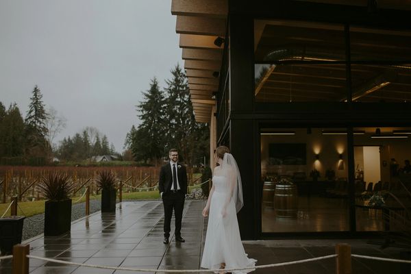 Bride and groom share a moment outside a modern building on a rainy day.