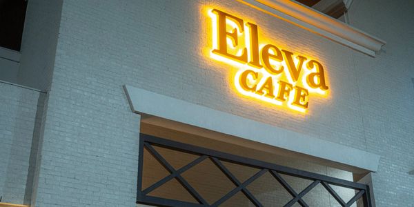 Glowing yellow sign for Eleva Cafe on a brick building facade at night.
