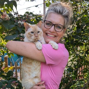 Woman in glasses hugging a large orange cat outdoors.