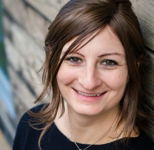Smiling woman with brown hair leaning against a wall.