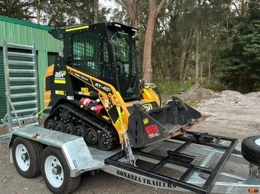 Compact ASV RT-40 tracked loader on a Bonanza trailer in a wooded area.
