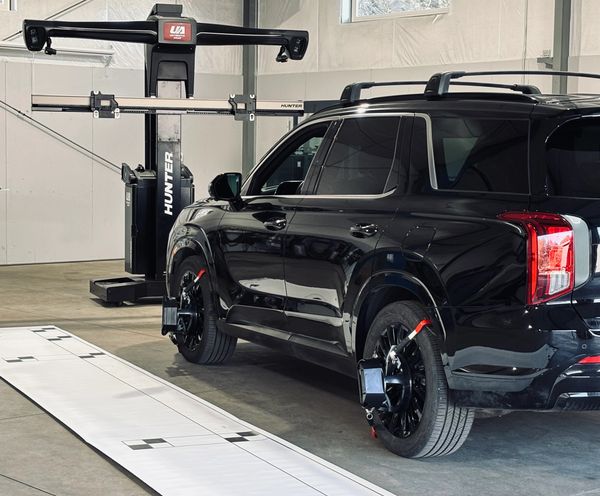 Black SUV undergoing wheel alignment with calibration equipment.