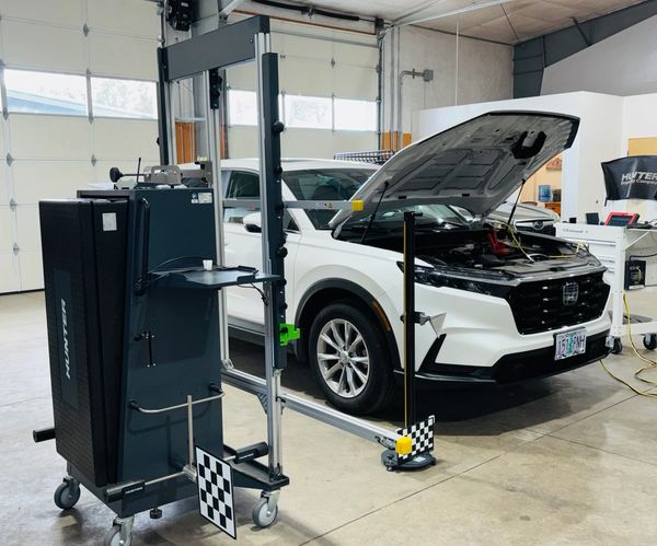 White SUV with open hood inside a garage, surrounded by automotive diagnostic equipment.