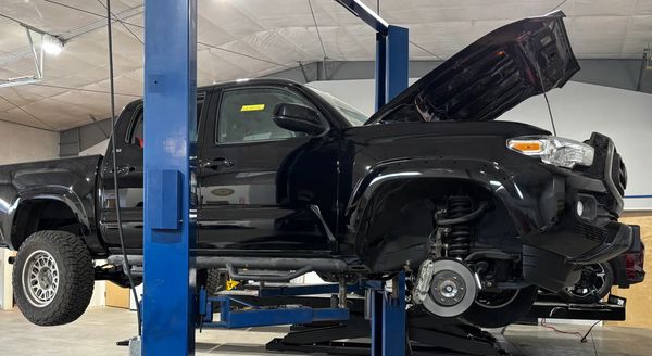 Black pickup truck lifted with hood open and front wheel removed in a garage.